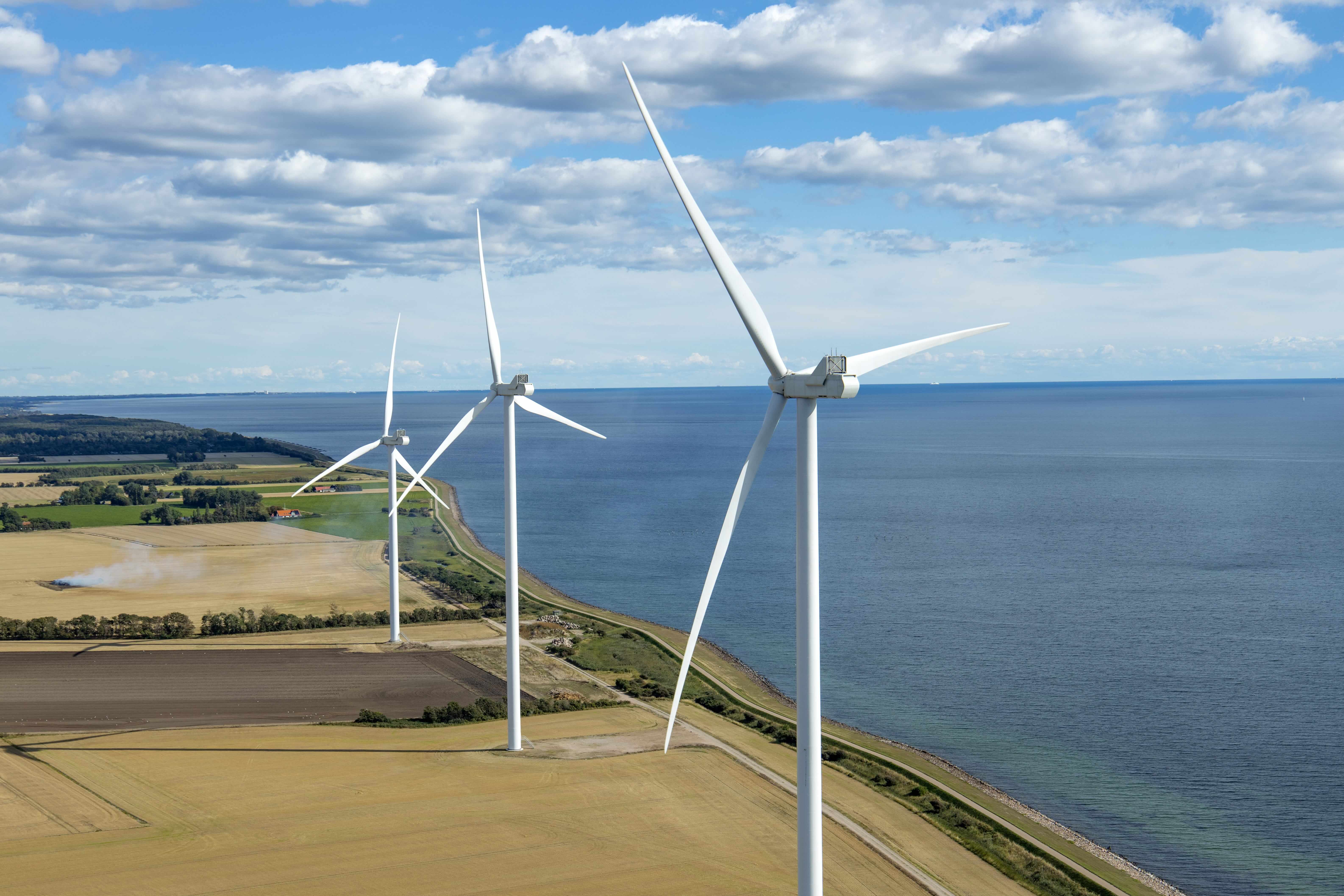 Drei Windr�der an einer K�ste neben Feldern, im Hintergrund das Meer und ein wolkiger Himmel